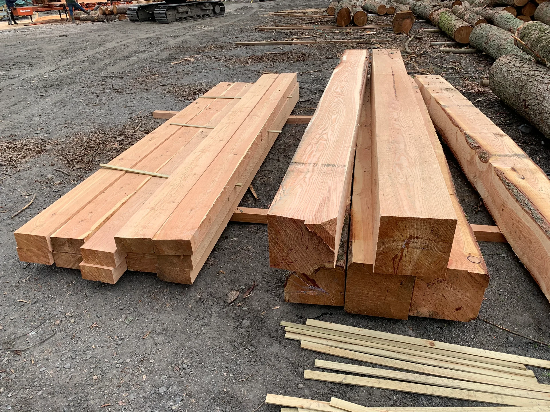 Stacks of freshly milled timber beams at a sawmill, showing the use of local materials in sustainable construction.