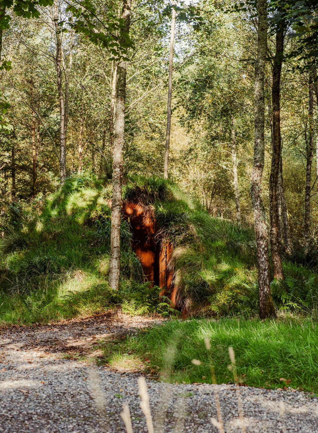 Earth-covered woodland shelter with a rusted metal entrance, integrated into the landscape to reduce visual and environmental impact.