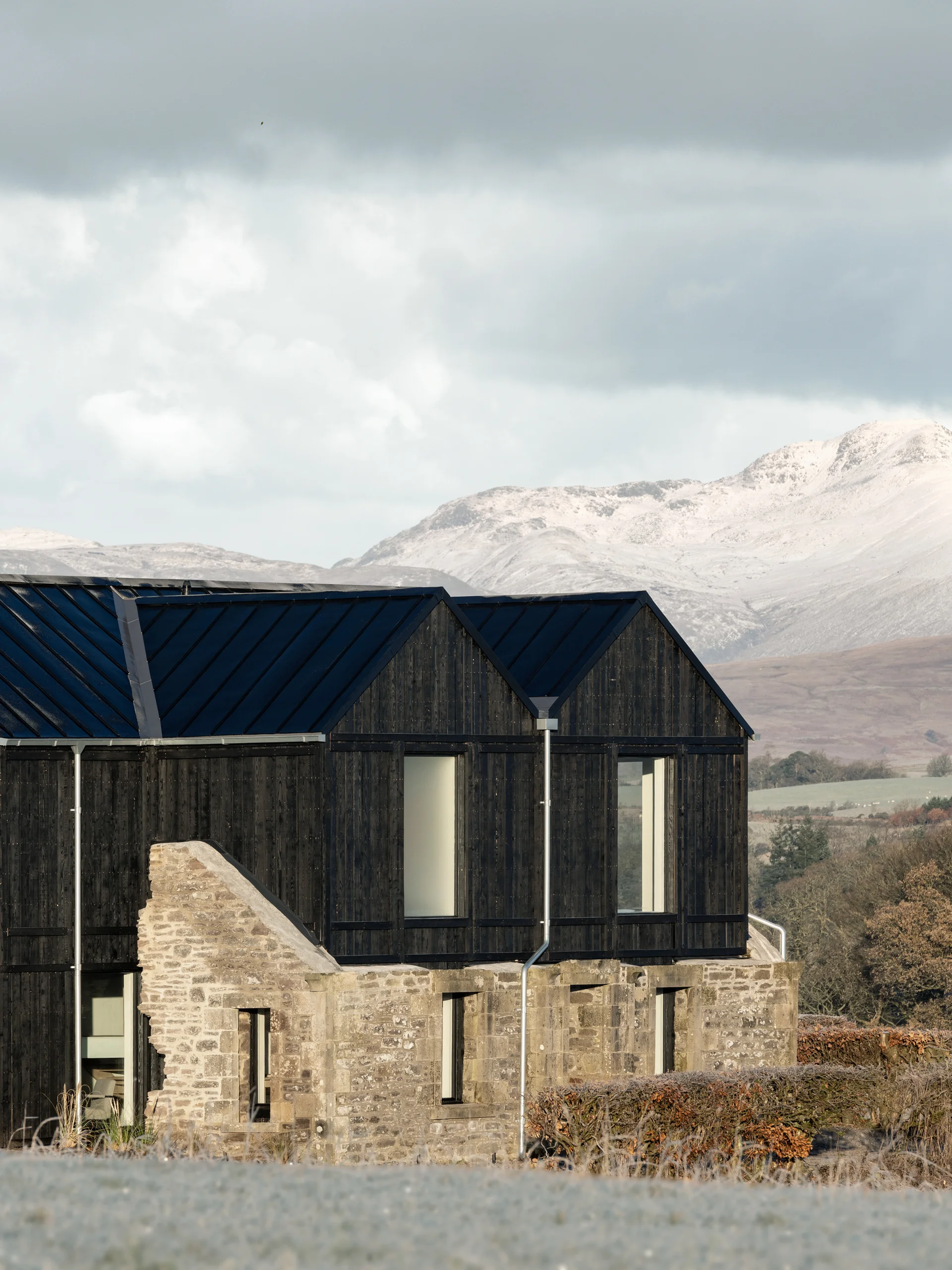 Contemporary home with blackened timber cladding atop a retained stone structure, demonstrating adaptive reuse in a rural setting.