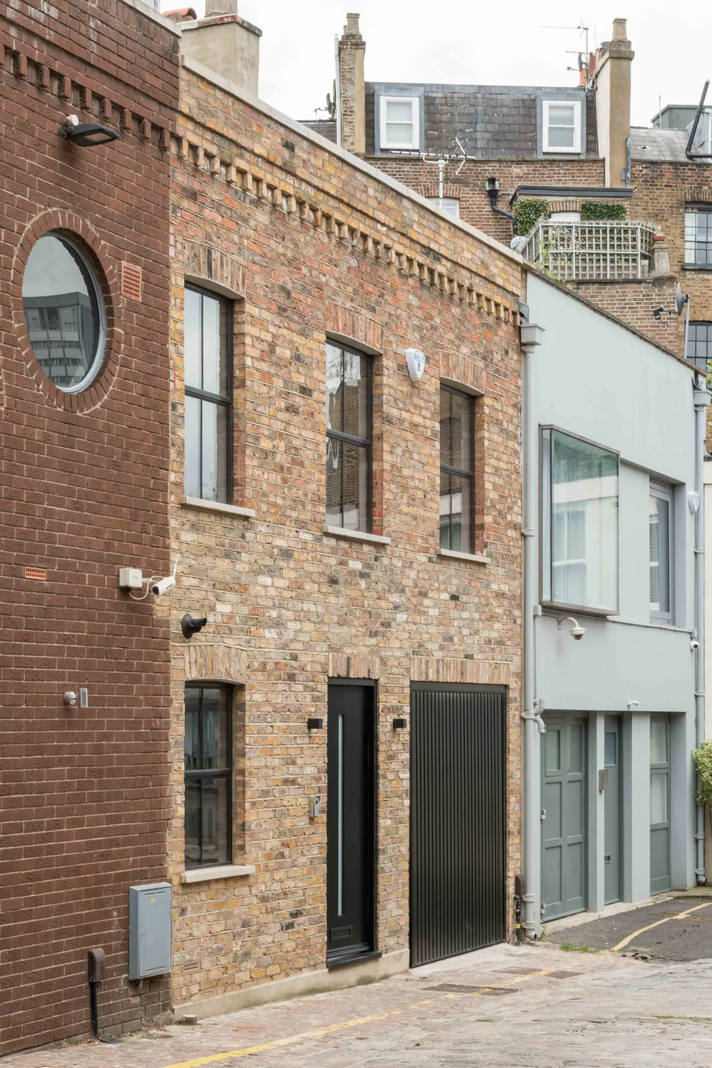 Exterior of a renovated brick mews house with black-framed windows, modern garage door, and contrasting brick textures.