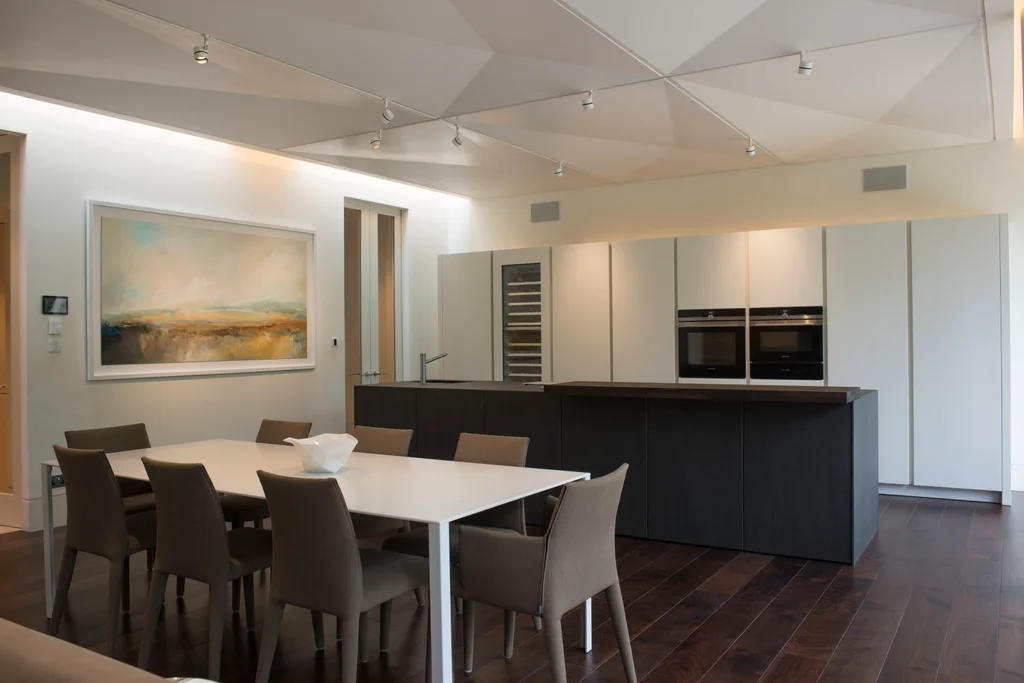 Modern open-plan kitchen and dining area with minimalist cabinetry, a black island, dining table, and contemporary artwork.