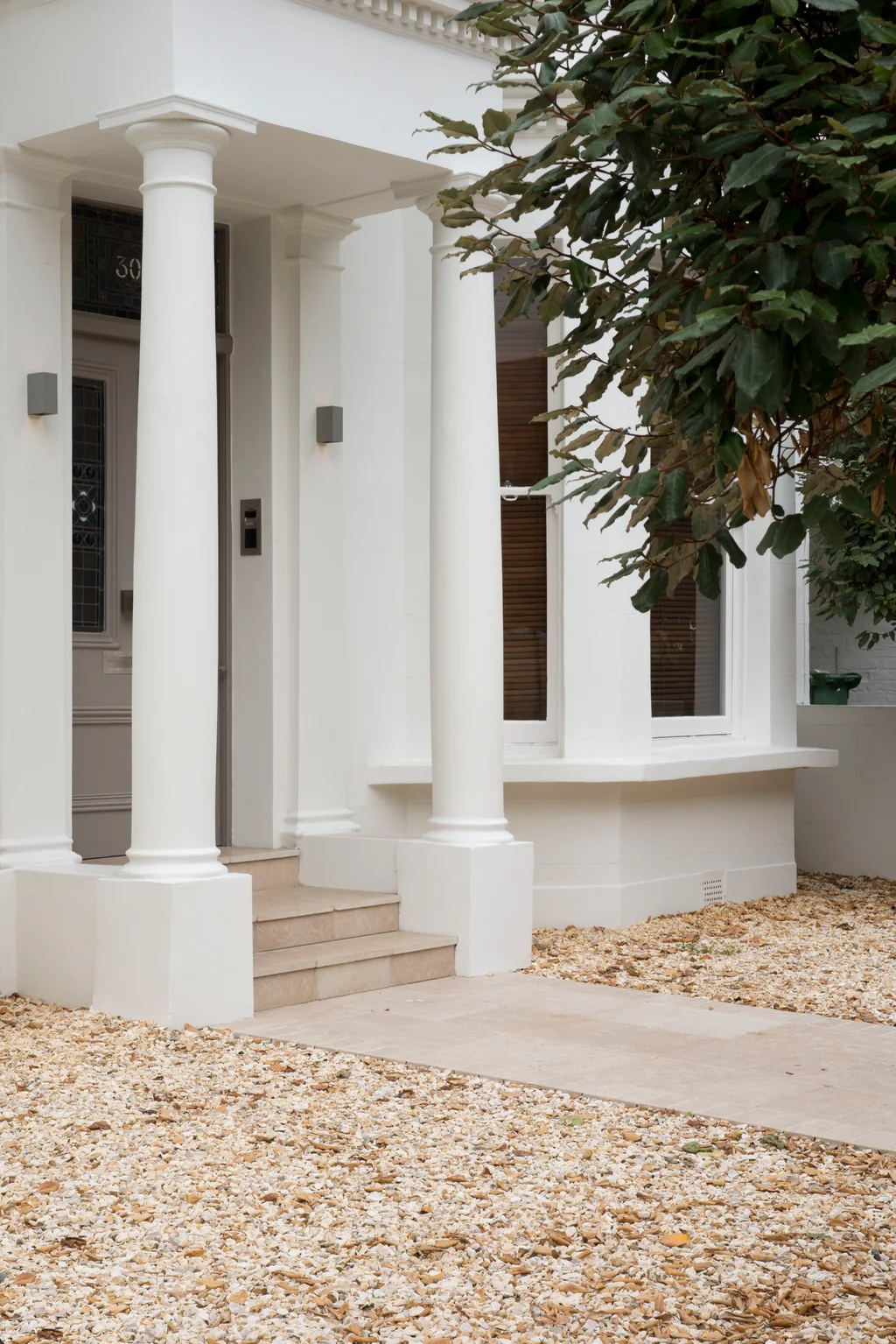 White-painted townhouse entrance with tall columns, stone steps, and gravel landscaping.