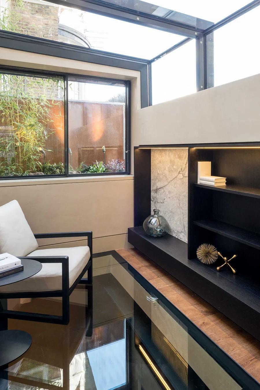 Bright indoor seating area with glass walls, modern shelving, and natural light from a glass roof.