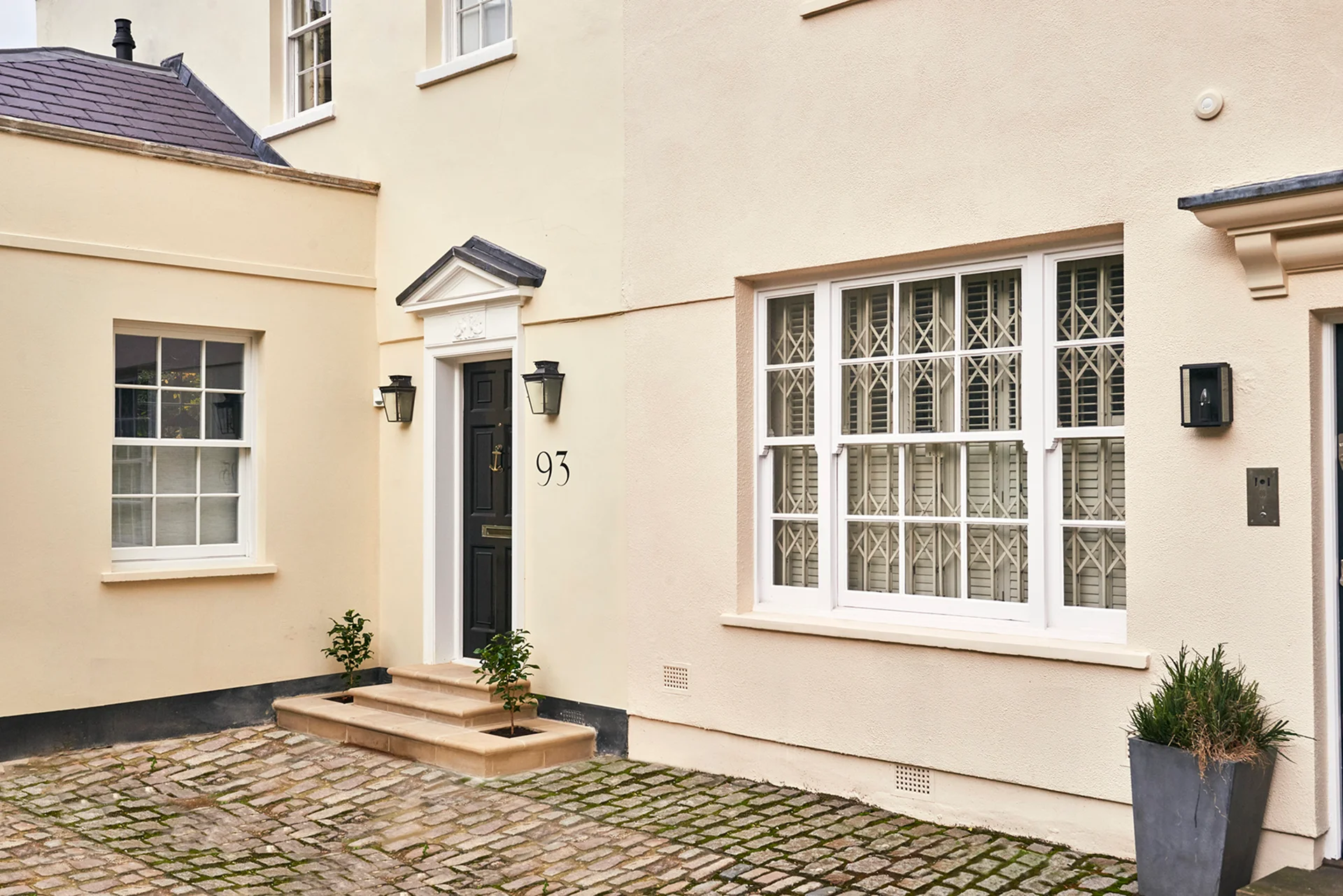 Cream-painted townhouse with black front door, cobblestone courtyard, and white-framed windows.