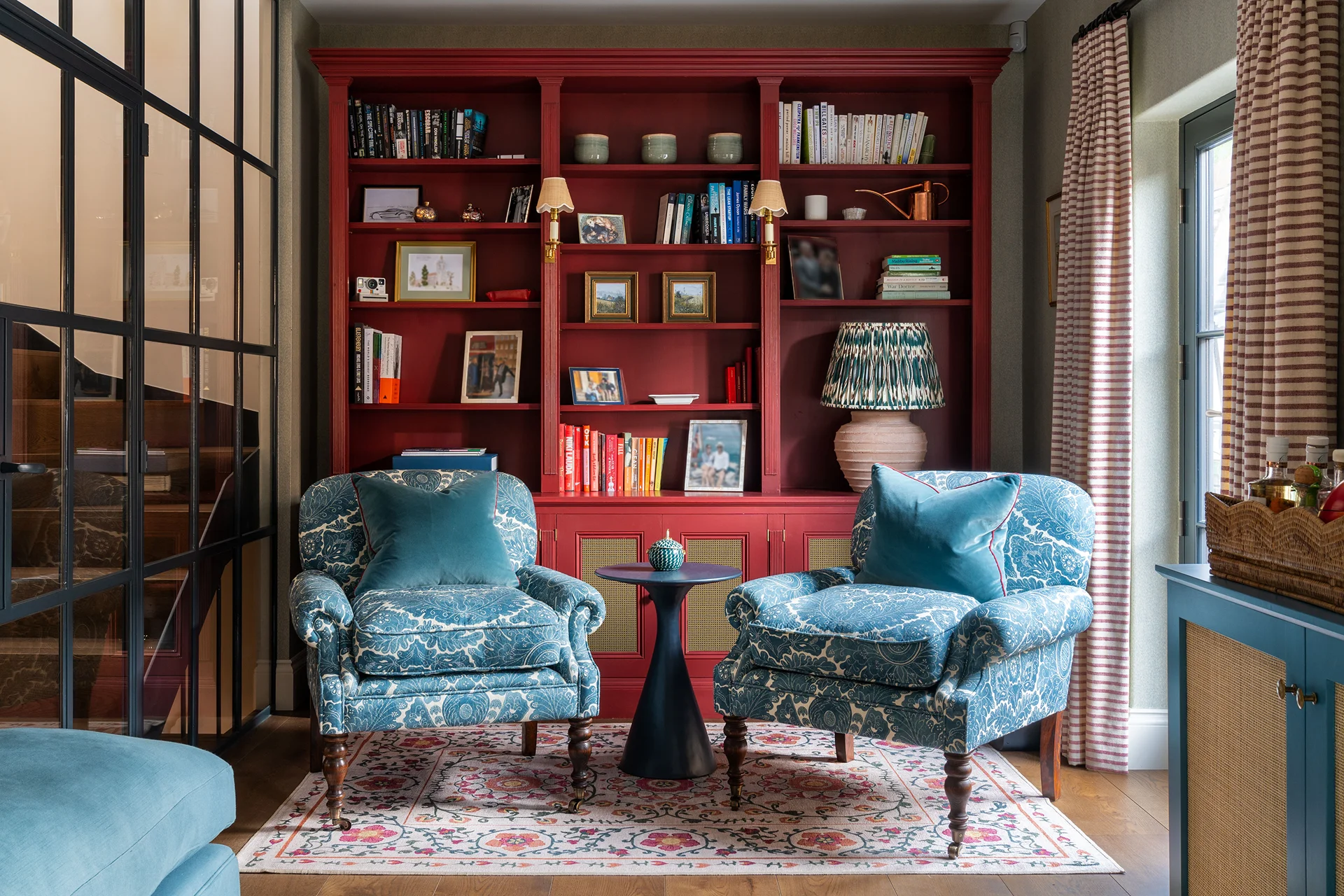 Cosy sitting room with teal patterned armchairs, a red built-in bookcase, and warm lighting creating a homely atmosphere.
