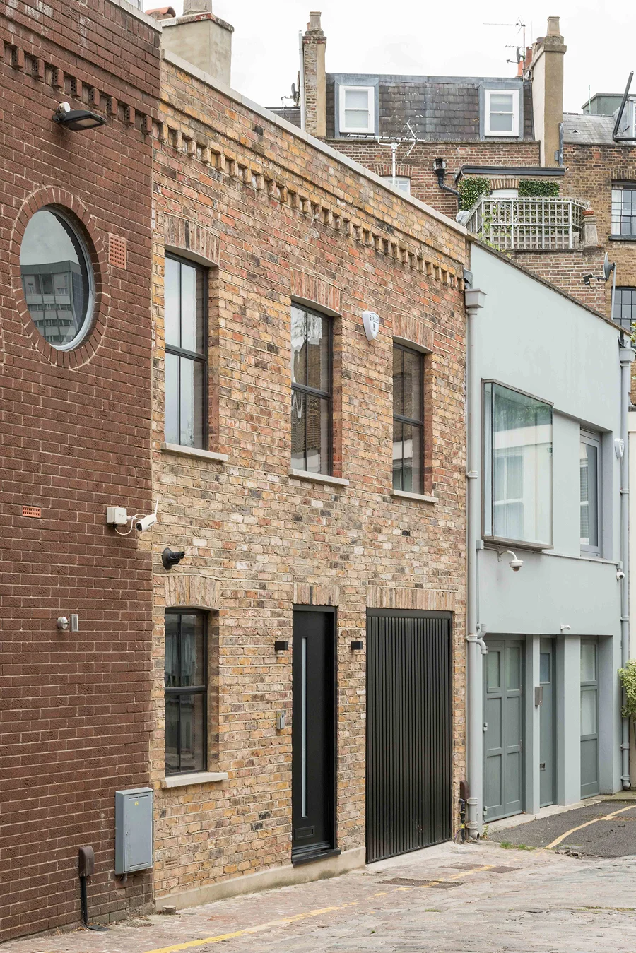 Converted mews house with exposed brick façade, black-framed windows, and a modern black door and garage entrance.