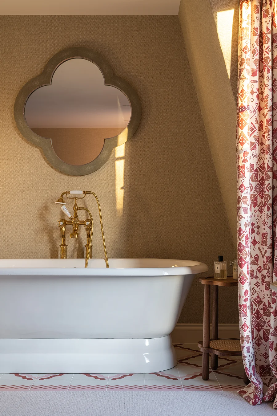 Elegant bathroom with freestanding white bathtub, brass fixtures, and a quatrefoil mirror above textured beige walls.