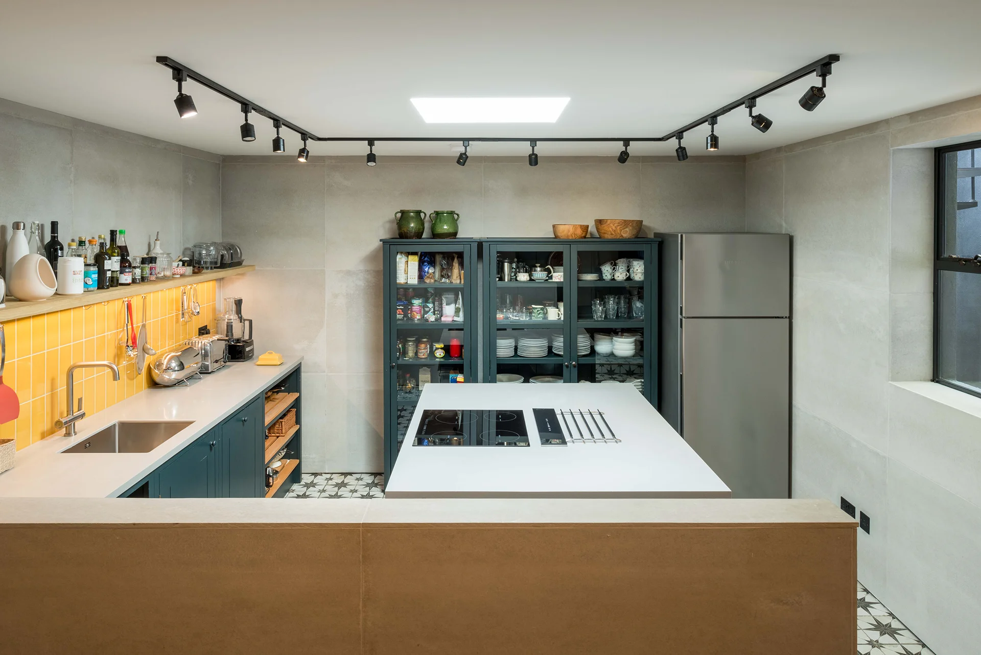 Contemporary kitchen featuring deep blue cabinetry, bright yellow tiled backsplash, and a central island with induction hob.