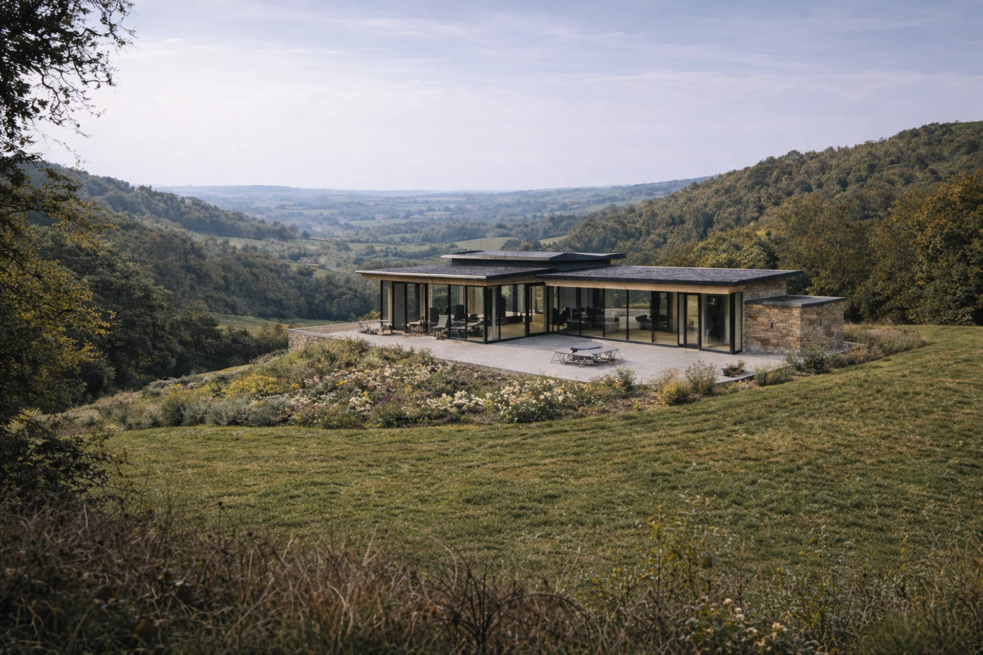 Modern house with large windows, surrounded by greenery and hills under a cloudy sky.