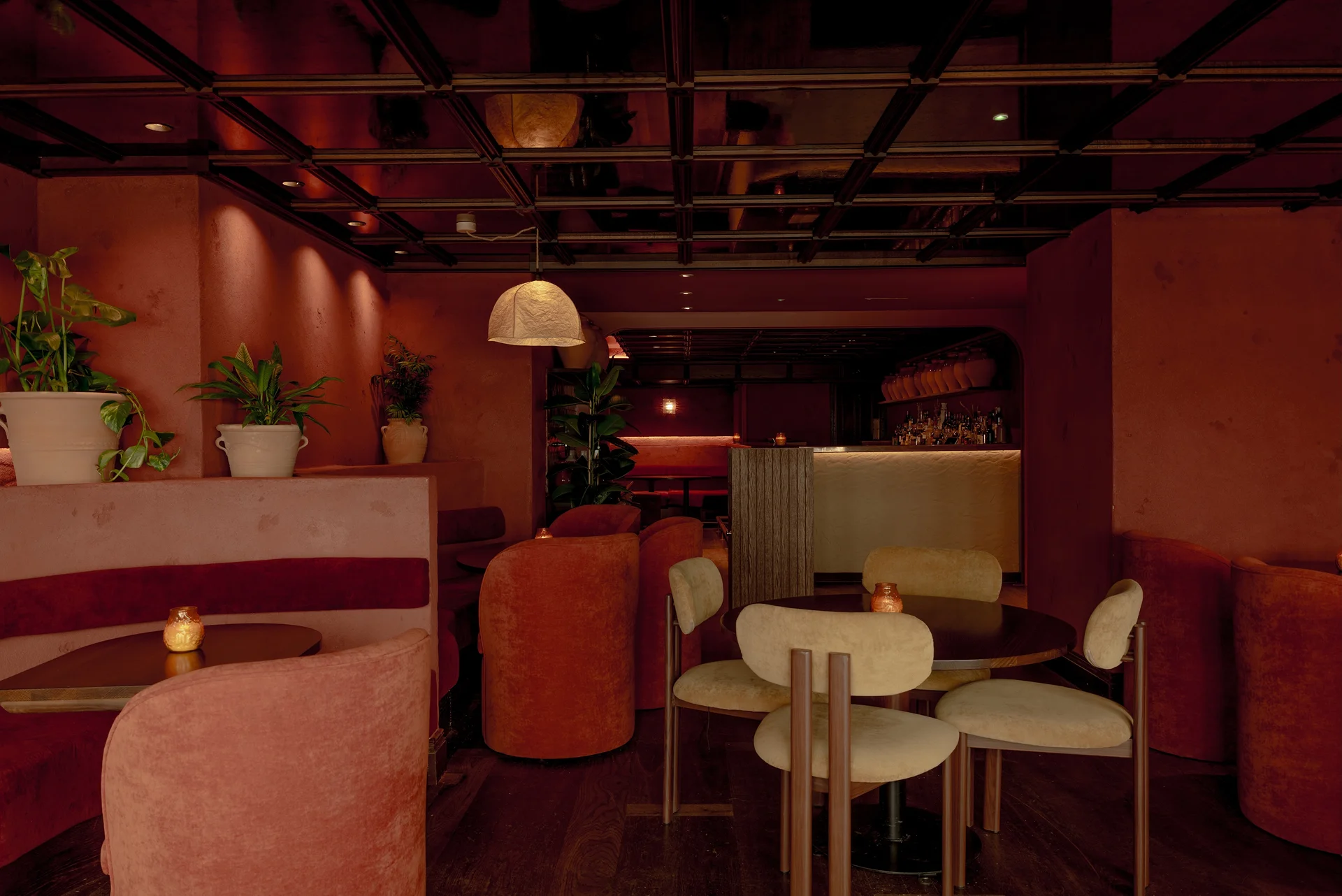 Cozy restaurant interior with soft pink walls, round tables, and stylish seating arrangements. Plants and warm lighting