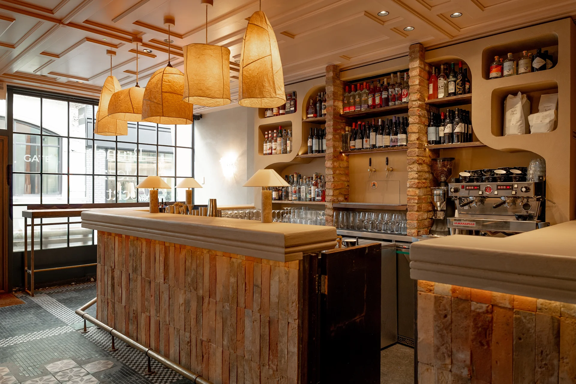 Stylish restaurant interior with a wooden bar, hanging lamps, and shelves stocked with bottles and glasses.