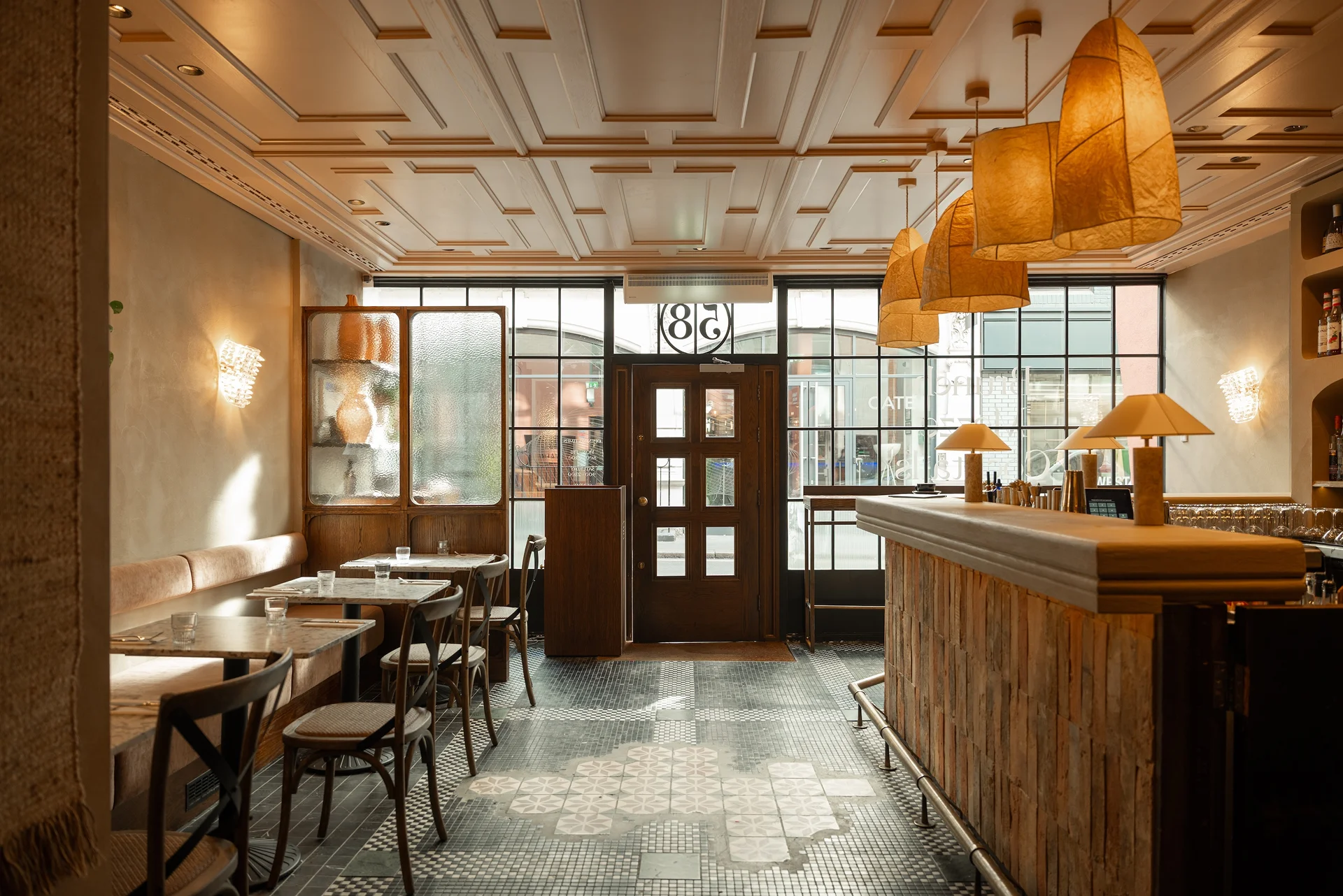 Interior of a cozy restaurant featuring wooden furniture, pendant lamps, and large windows allowing natural light.